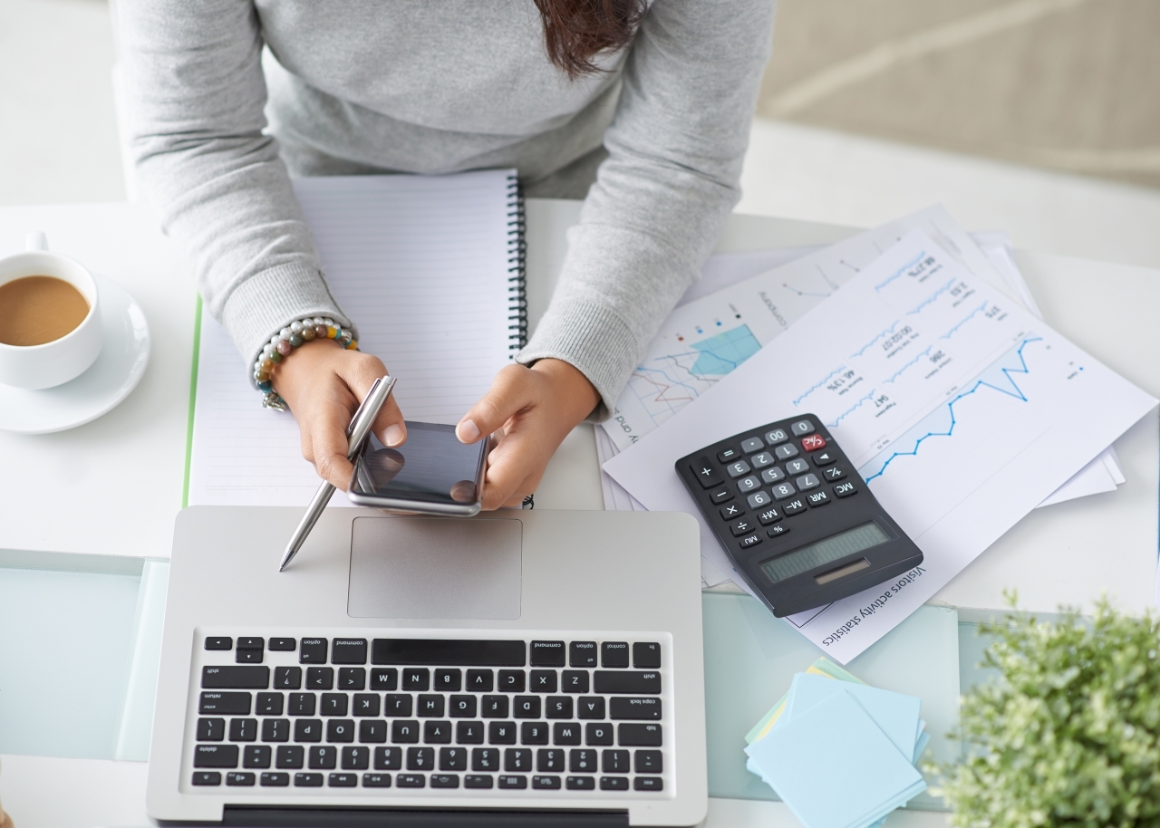 Woman at desk with phone, laptop, calculator, and financial documents